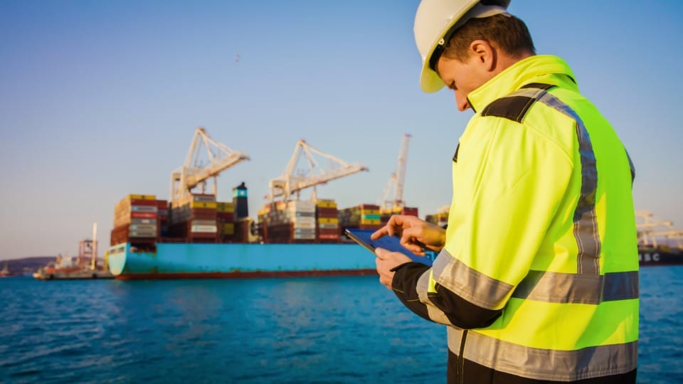 worker in protective gear working on tablet computer in front of container terminal