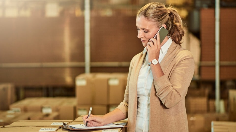 supervisor taking notes on a clipboard, talking on a mobile phone in a warehouse