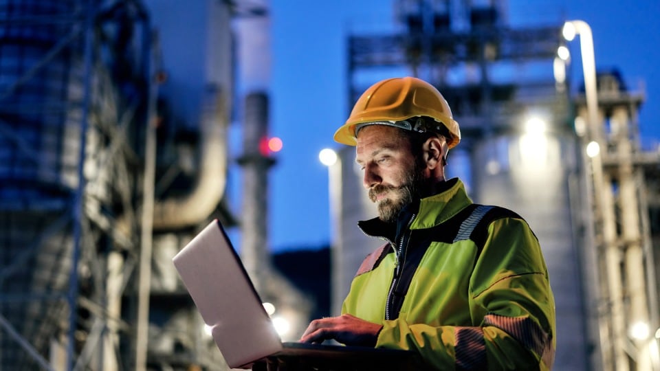 Engineer wearing a hard hat using a laptop outside 