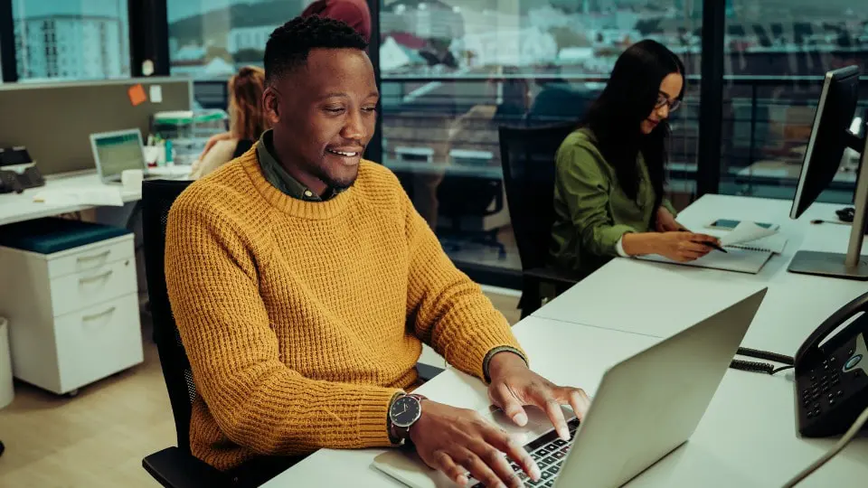 Business professional typing on a laptop sitting next to co-worker